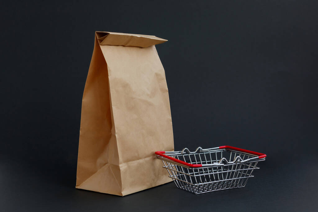 brązowa papierowa torba na zakupy na czarnym tle i mały koszyk spożywczy - Zdjęcie, obraz