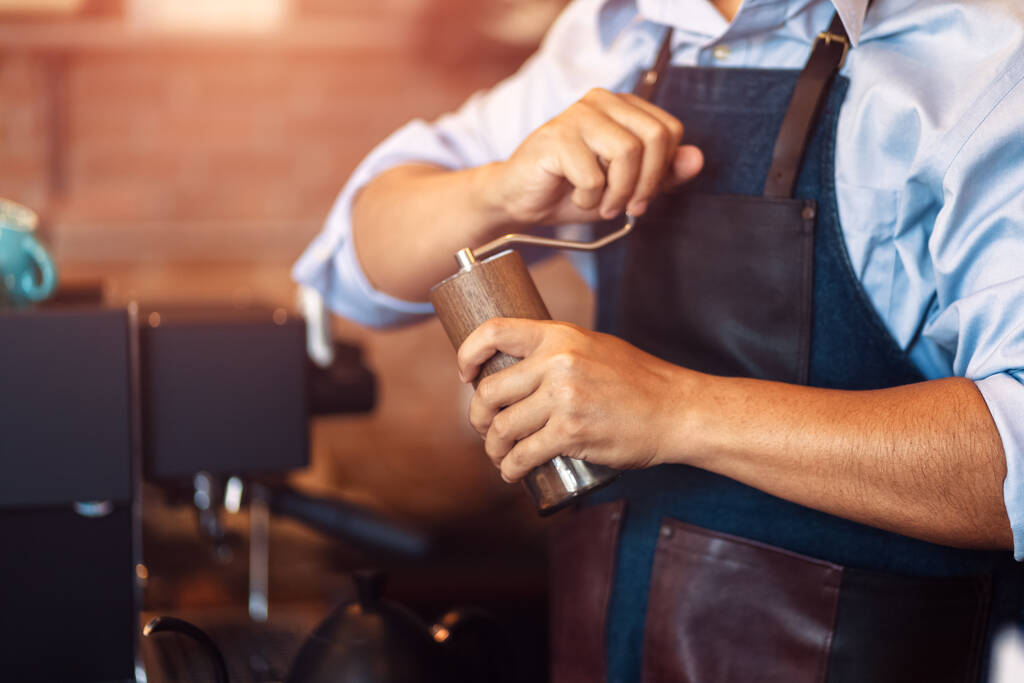 a barista kezét a kézi csiszoló kávé őrlésére kávébab kávézóban. - Fotó, kép