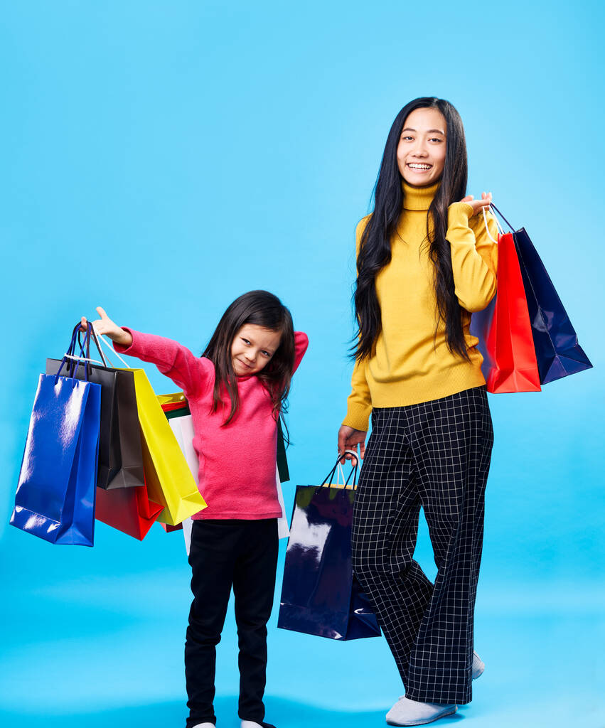 Щаслива мати з чарівною маленькою дочкою, що тримає сумки, насолоджується їх покупкою на синьому фоні
 - Фото, зображення