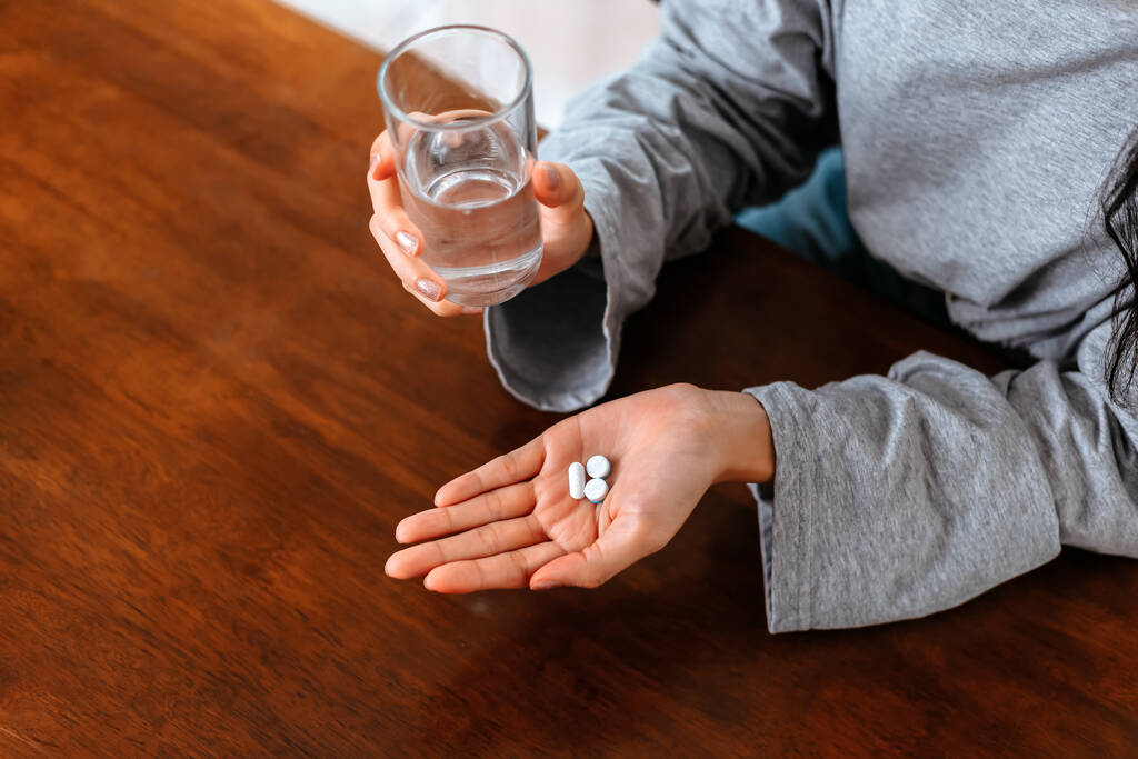 Empresárias que trabalham em casa com vidro de água leva pílula redonda branca na mão
. - Foto, Imagem