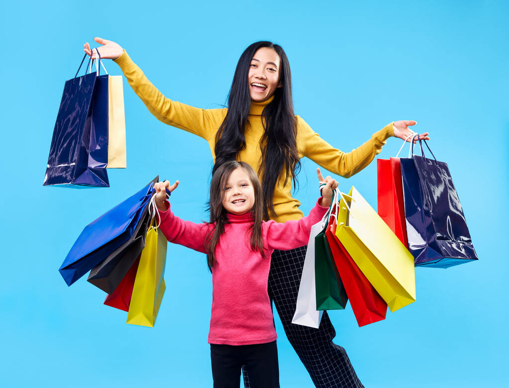 Felice madre con adorabile figlioletta che tiene borse della spesa godere il loro acquisto su sfondo blu
. - Foto, immagini