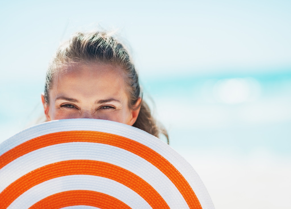 Happy young woman in swimsuit hiding behind beach hat - Photo, Image