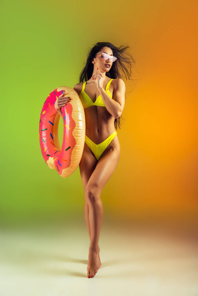 Модний портрет молодої посадки та спортивної жінки з гумовим пончиком у стильному жовтому купальнику на градієнтному фоні. Ідеальне тіло готове до літнього часу
. - Фото, зображення
