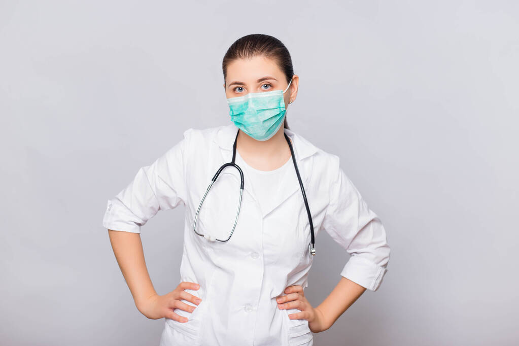Γιατρός κορίτσι σε ένα λευκό παλτό και ιατρική μάσκα με στηθοσκόπιο απομονώνονται σε λευκό φόντο. - Φωτογραφία, εικόνα