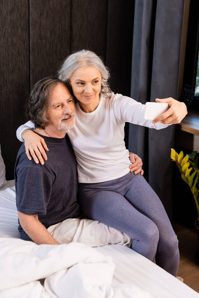 mature woman taking selfie with husband in bedroom  - Photo, Image
