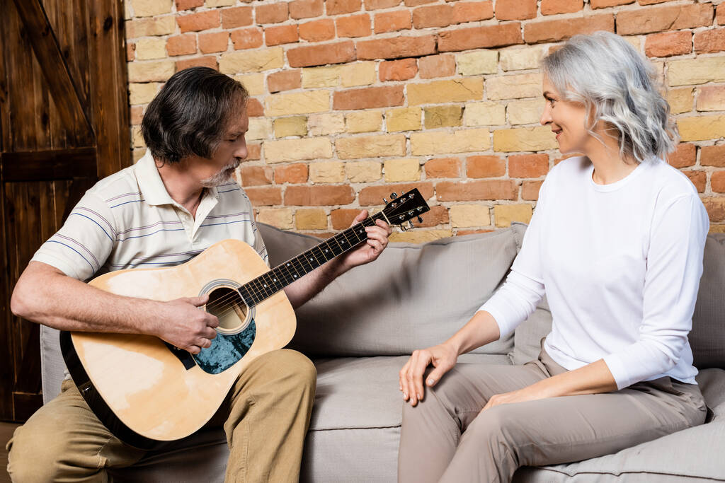 barbudo y maduro hombre jugando guitarra acústica cerca feliz esposa
  - Foto, Imagen