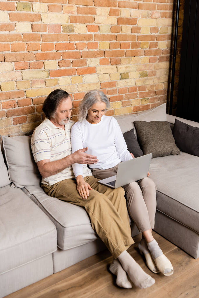 чоловік середнього віку вказує рукою на ноутбук біля дружини
  - Фото, зображення