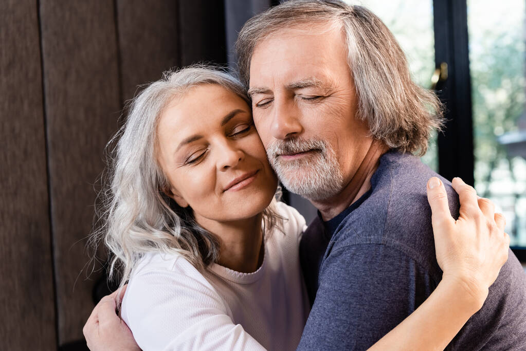 boldog középkorú pár csukott szemmel otthon ölelkezve - Fotó, kép