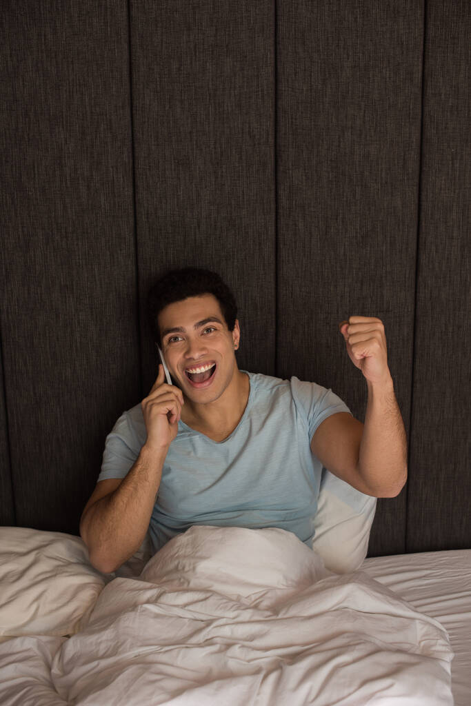 Aufgeregter Mischlingsmensch spricht während Selbstisolierung im Bett auf Smartphone - Foto, Bild
