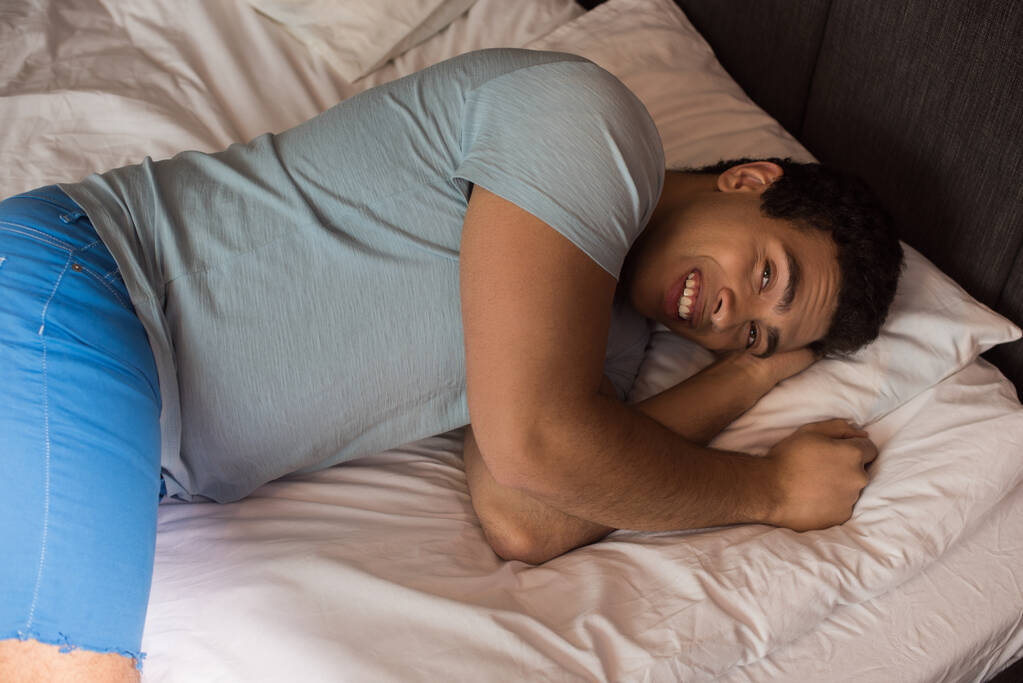 sonriente hombre de raza mixta acostado en la cama durante la cuarentena
 - Foto, imagen