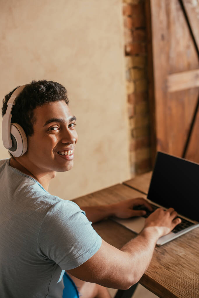 homme bi-racial souriant écoutant de la musique avec des écouteurs et utilisant un ordinateur portable pendant l'isolement personnel
 - Photo, image