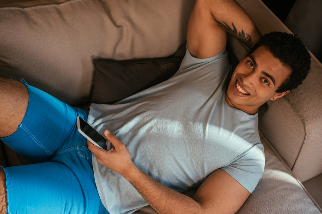 вид на счастливый смешанной расы человек охлаждения и использование смартфона на диване во время самоизоляции
  - Фото, изображение