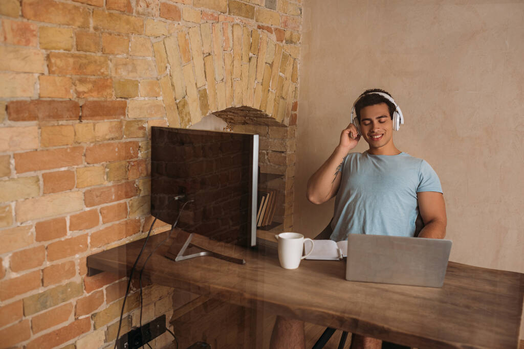 freelancer de raça mista sorridente em fones de ouvido trabalhando em home office durante quarentena
 - Foto, Imagem