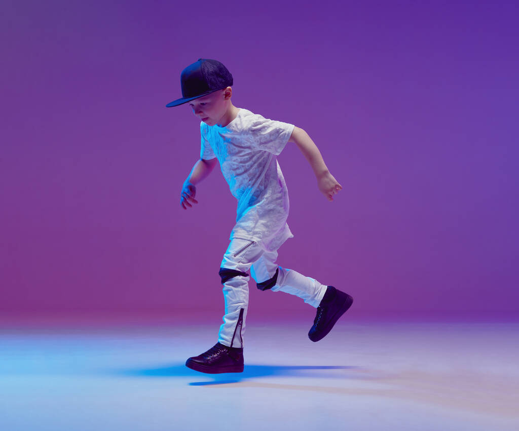Cooler kleiner Junge, der im Studio vor dem Hintergrund von Neonlicht Hip-Hop tanzt. Breakdance-Plakat. - Foto, Bild