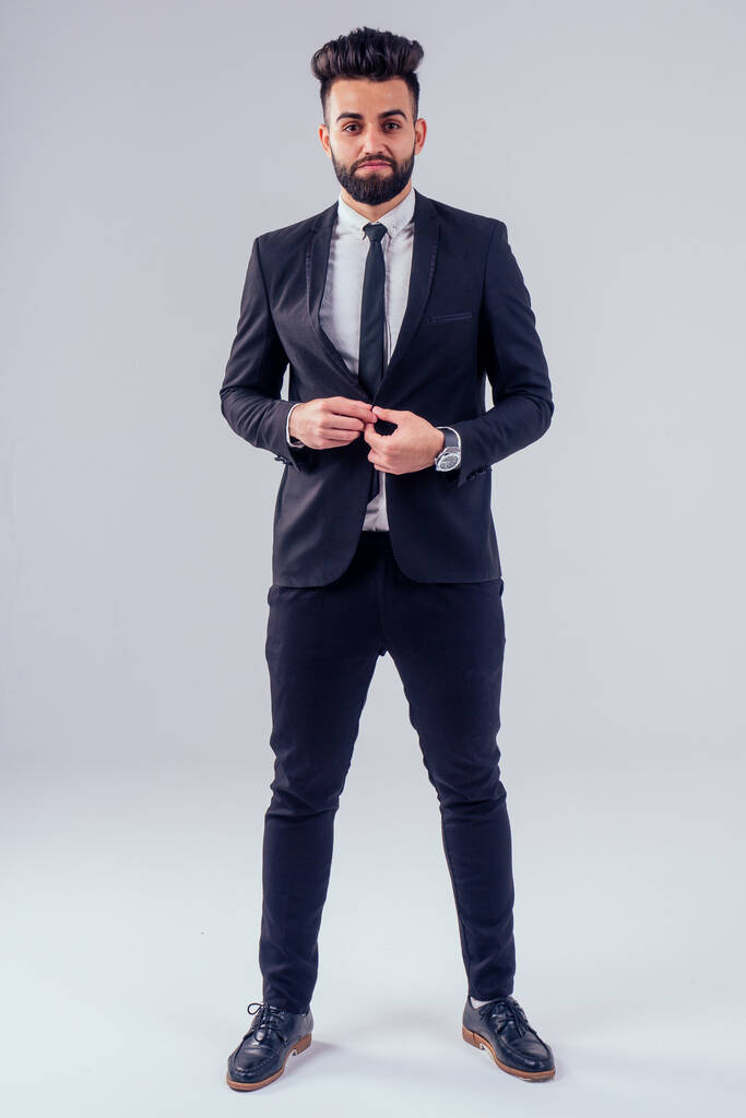 молодой турецкий красивый черный волосатый мужчина в стильном деловом костюме завязывая галстук в студии изолировать белый фон
 - Фото, изображение