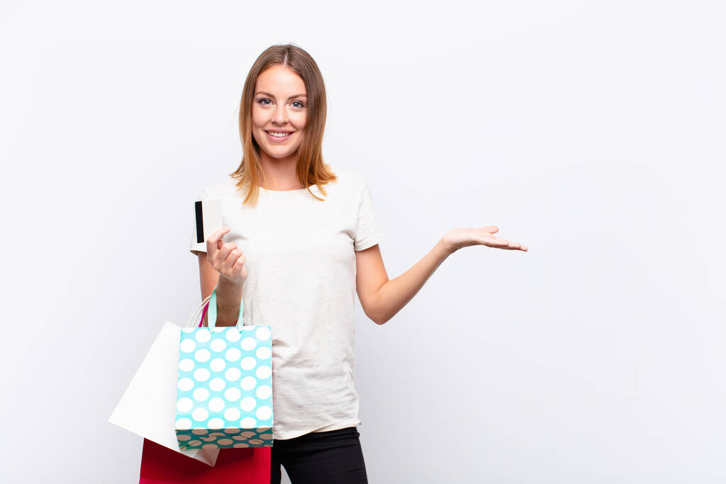 赤い頭の可愛い女が陽気に笑って幸せを感じショッピングバッグで手の手のひらでコピースペースでコンセプトを示す - 写真・画像