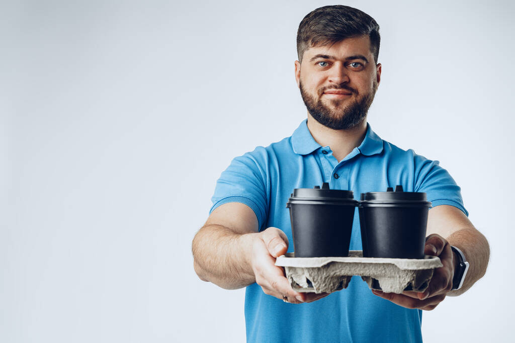 Hombre trabajador de la cafetería dando tazas de café para llevar sobre fondo gris
 - Foto, Imagen