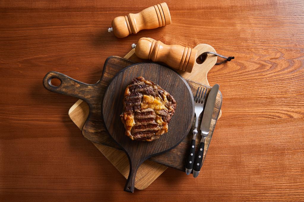 vue de dessus du délicieux steak grillé servi sur des planches de bois avec couverts, moulins à sel et poivre
 - Photo, image