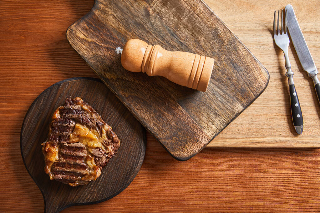 Blick von oben auf leckeres Steak vom Grill serviert auf Holzbrettern mit Besteck und Salz mil - Foto, Bild