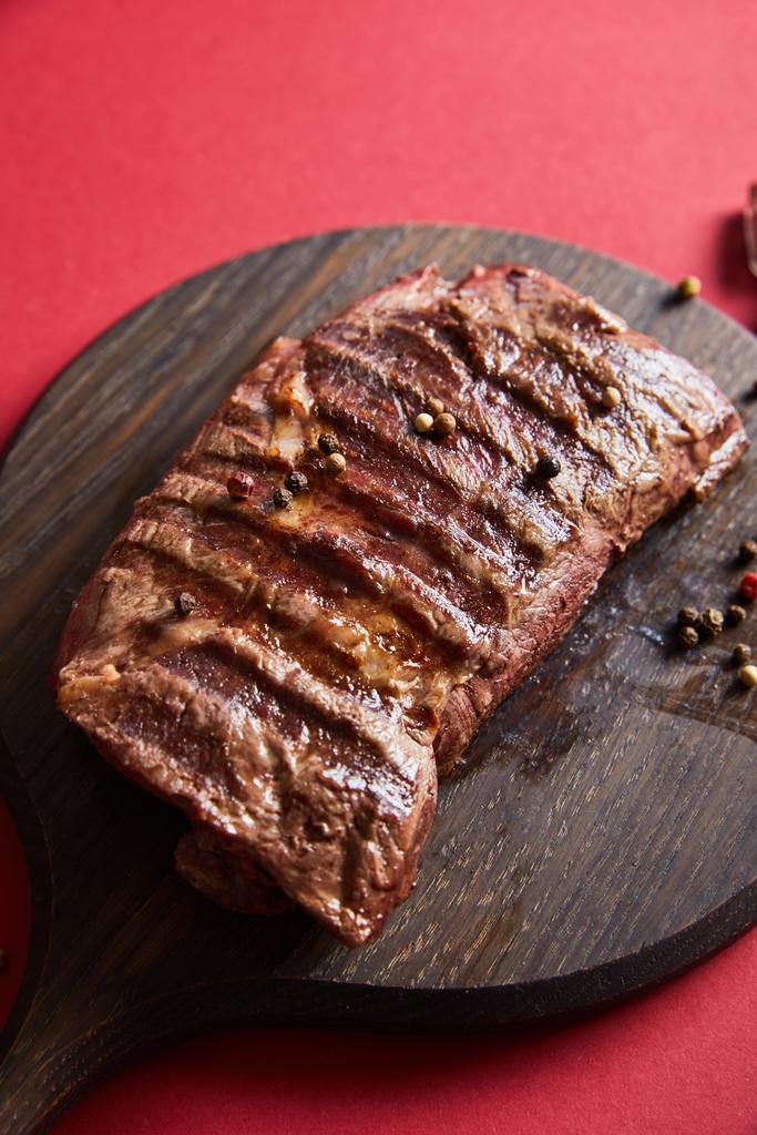 gustosa bistecca grigliata servita su assi di legno su fondo rosso con pepe
 - Foto, immagini