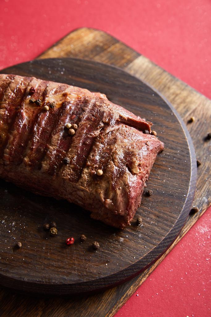 tasty grilled steak served on wooden boards on red background with pepper and salt - Photo, Image