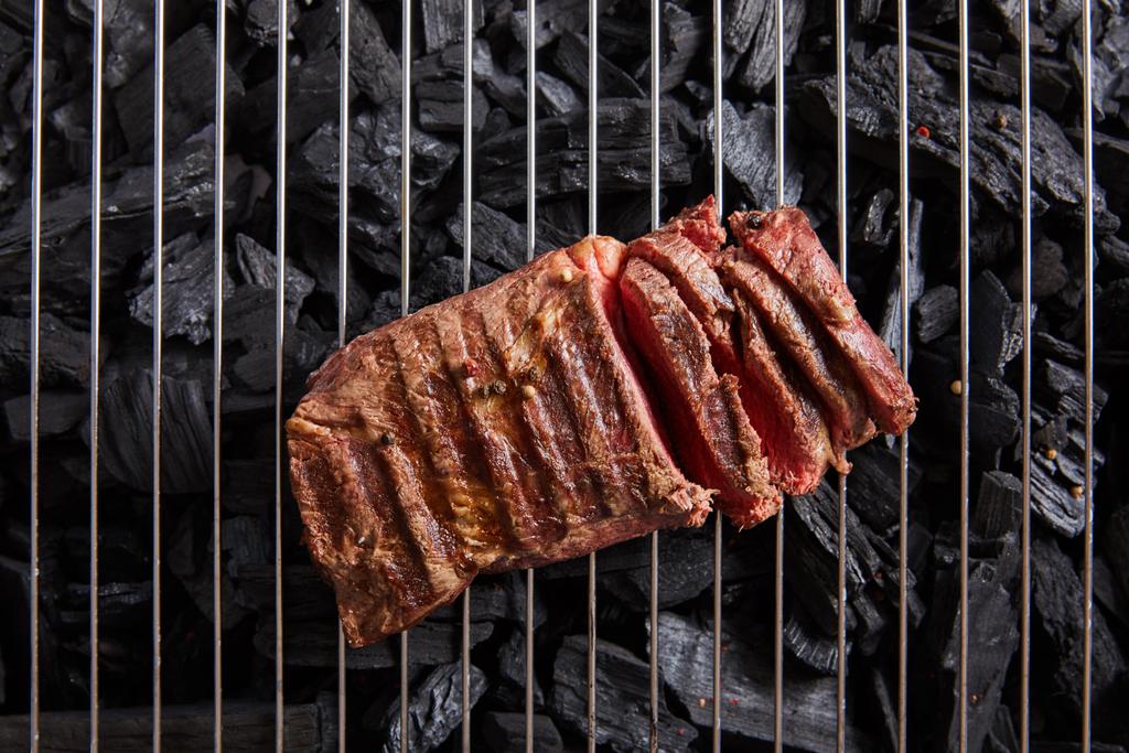 bovenaanzicht van gesneden verse gegrilde smakelijke biefstuk met zeldzame roosteren op rooster boven zwarte kolen - Foto, afbeelding