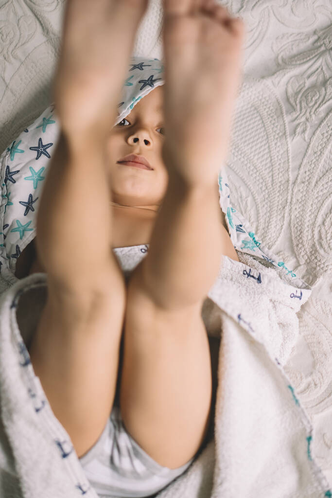 top view of adorable boy lying on bed with legs up and looking at camera - Photo, Image