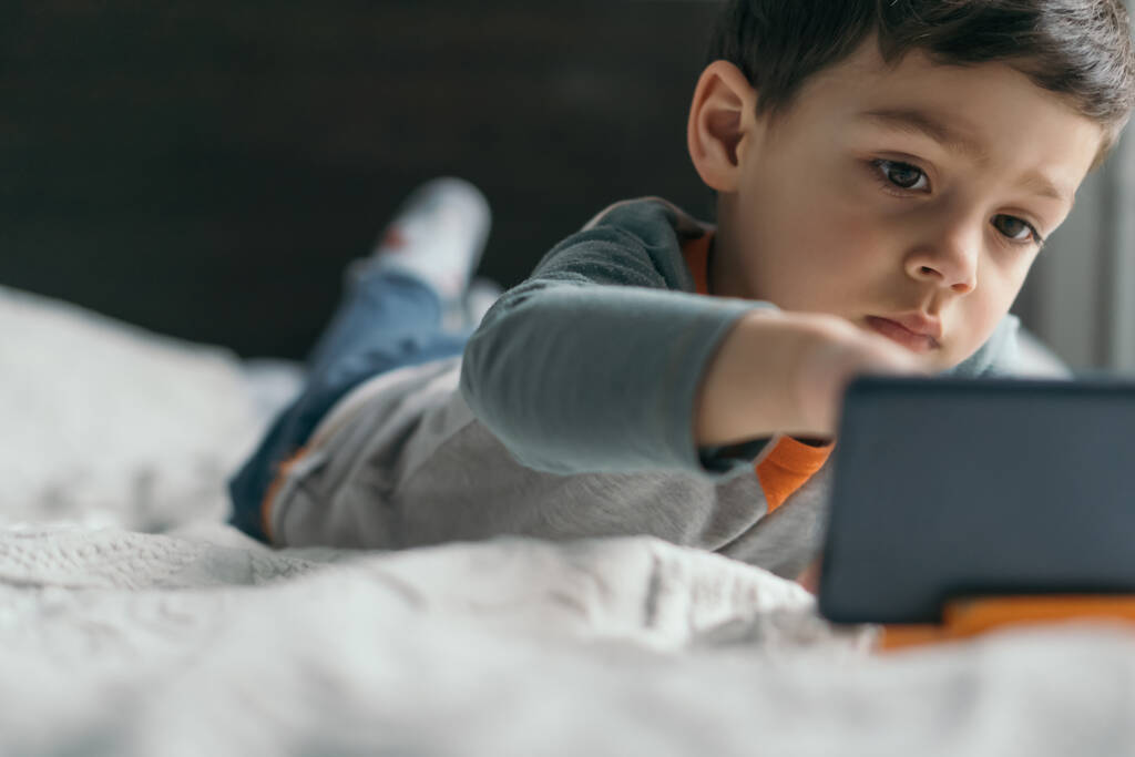 Yatakta yatarken akıllı telefona dokunan tatlı bir çocuğun seçici odağı. - Fotoğraf, Görsel