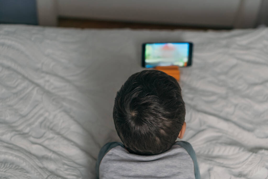 shora pohled na dítě sledování online lekce při ležení na posteli - Fotografie, Obrázek