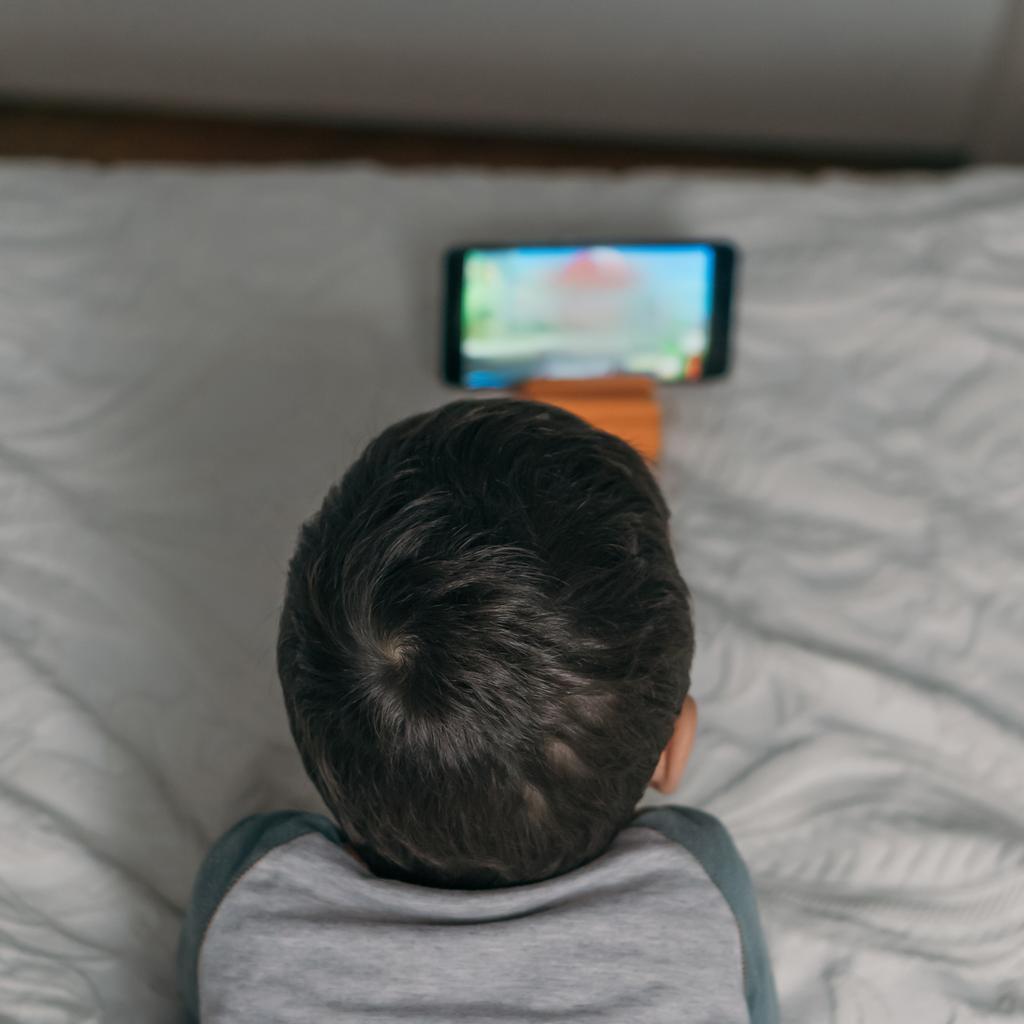 Overhead-Ansicht des Jungen, der auf dem Smartphone eine pädagogische Karikatur anschaut, während er auf dem Bett liegt - Foto, Bild