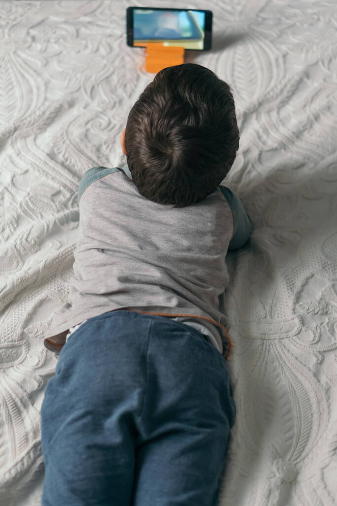vista superior do menino assistindo webinar no smartphone enquanto deitado na cama
 - Foto, Imagem