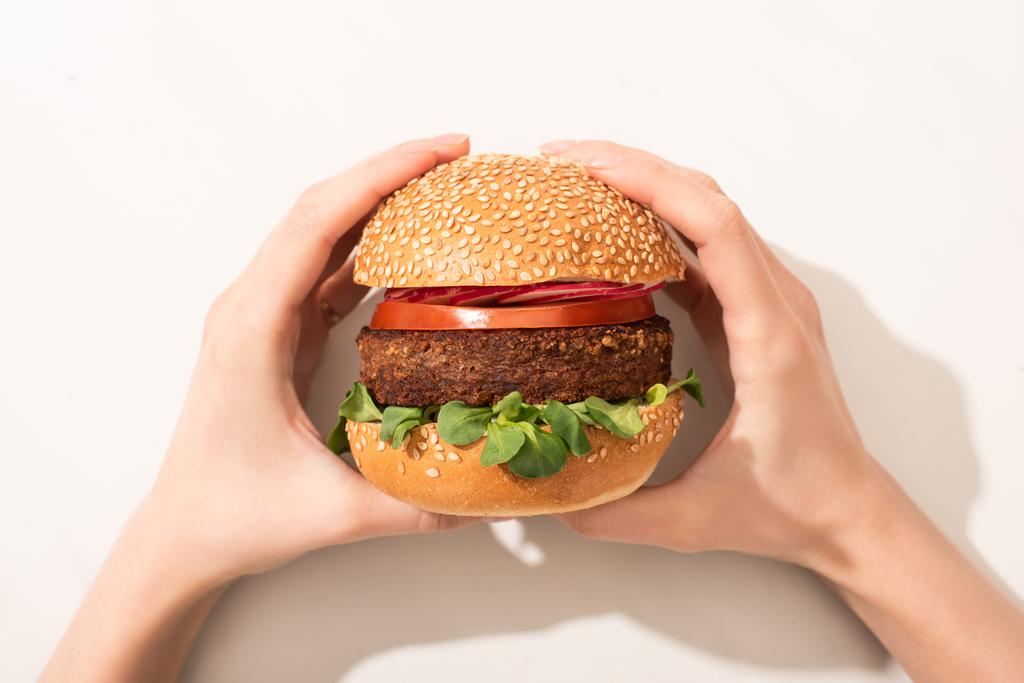 vista cortada de mulher segurando delicioso hambúrguer vegan com rabanete no fundo branco
 - Foto, Imagem