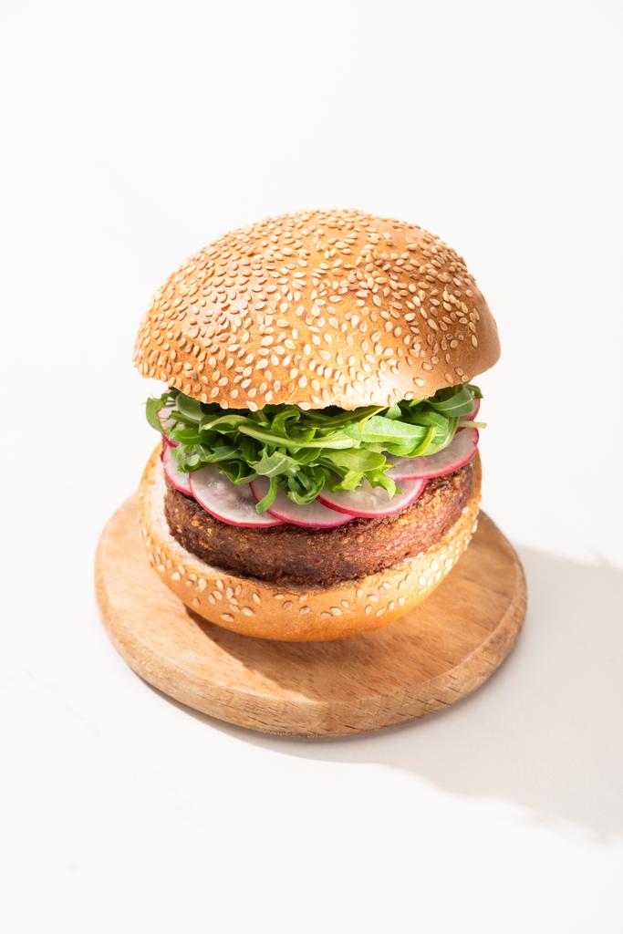 delicioso hambúrguer vegan com rabanete e rúcula em tábua de madeira no fundo branco
 - Foto, Imagem