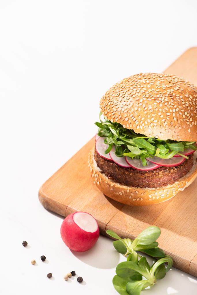 vynikající veganský burger s ředkvičkou a rukolou na dřevěné desce s černým pepřem na bílém pozadí - Fotografie, Obrázek