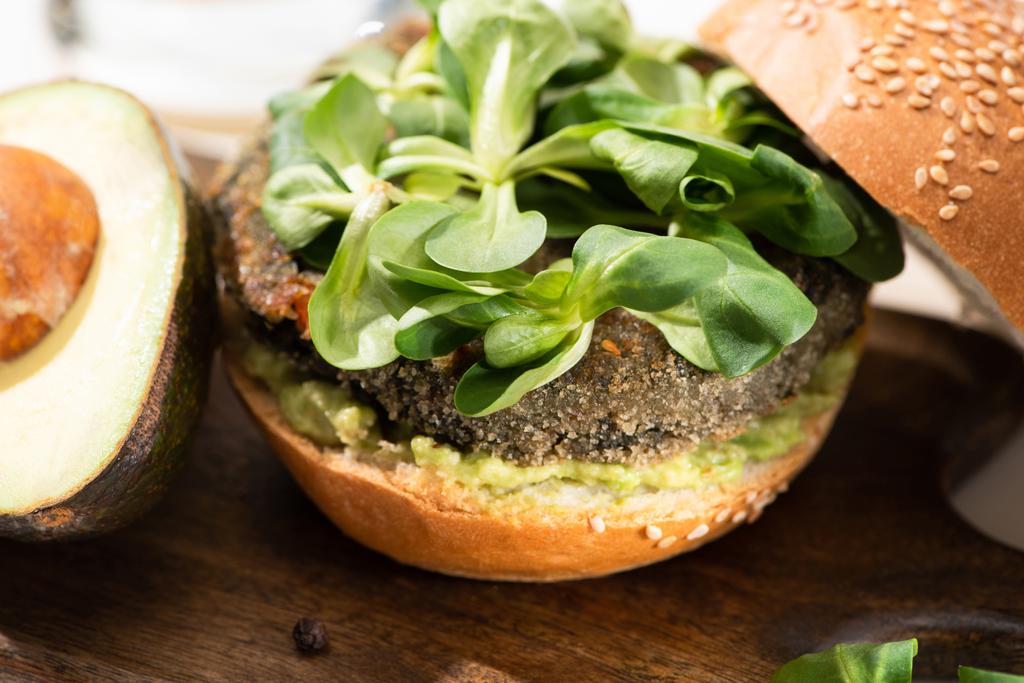 vista de cerca de la deliciosa hamburguesa verde vegana con microgreens, aguacate en la tabla de cortar de madera
 - Foto, imagen