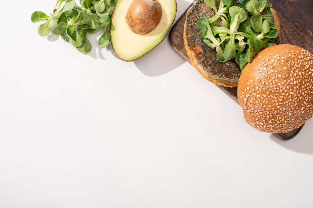 top view of vegan burger with microgreens and avocado on wooden cutting board on white background - Photo, Image