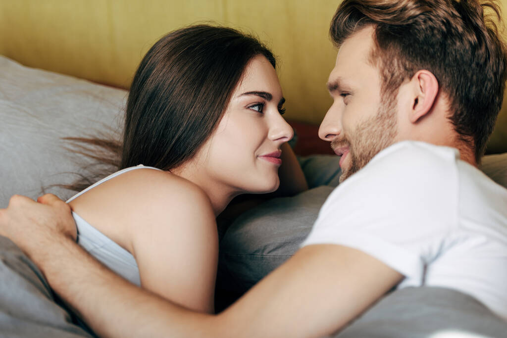 selektywne skupienie szczęśliwy mężczyzna i wesoły kobieta patrząc na siebie w łóżku  - Zdjęcie, obraz