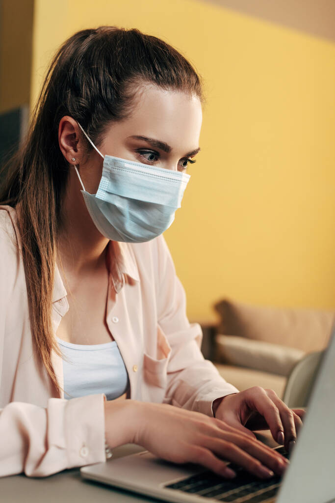 selective focus of freelancer in medical mask using laptop at home  - Photo, Image