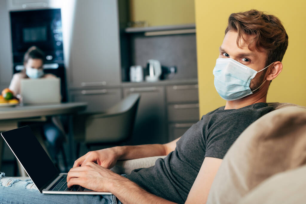 селективный фокус фрилансера в медицинской маске с использованием ноутбука с пустым экраном рядом с девушкой
  - Фото, изображение