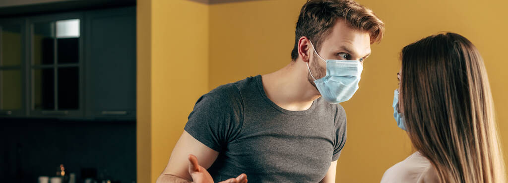 panoramic concept of couple in medical masks quarreling at home - Photo, Image