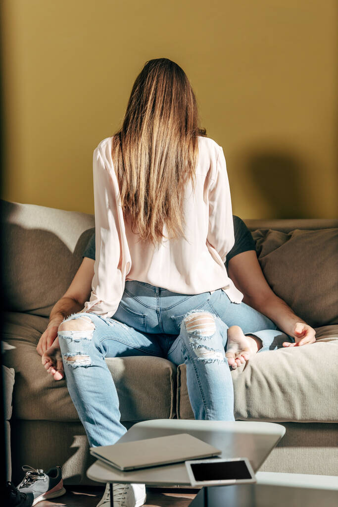 Rückansicht eines sinnlichen Mädchens, das auf einem Mann im Wohnzimmer sitzt  - Foto, Bild