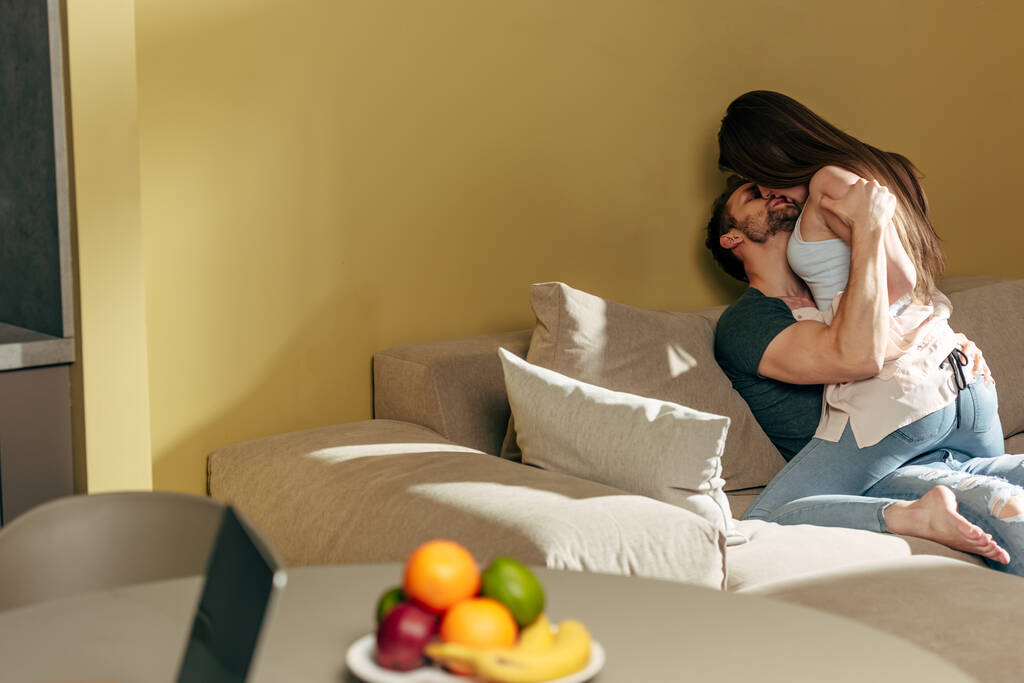 вибірковий фокус сексуальної пари цілується на дивані біля фруктів на столі
  - Фото, зображення
