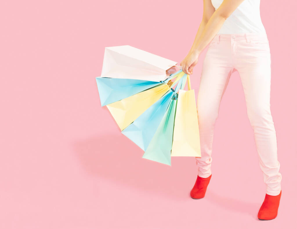 The female body part wore pink trousers and red boots. Carrying a shopping bag in many pastel colors on pink background selective focus,shopping concept - Photo, Image