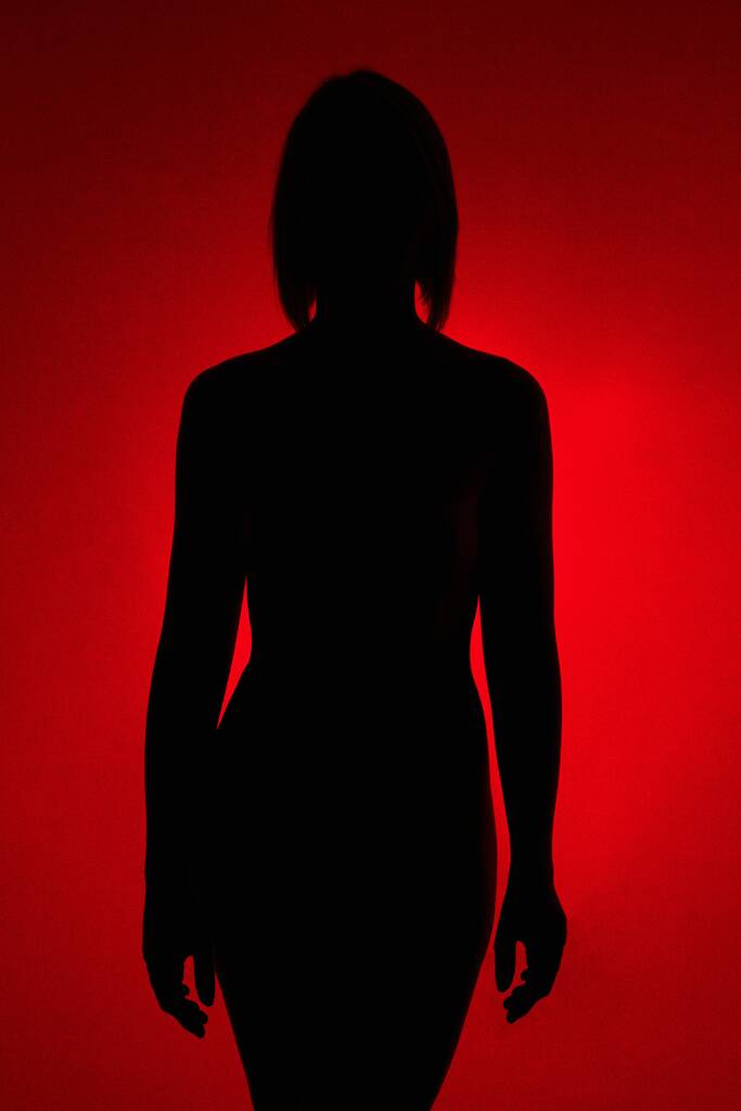 Eine vertikale Aufnahme der Silhouette einer Frau auf rotem Hintergrund - Foto, Bild