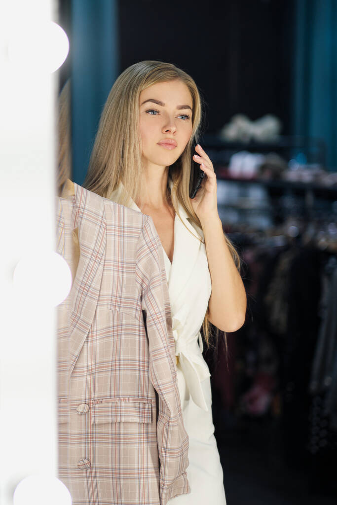 jong mooi blond vrouw probeert en kiest een jurk in een garderobe in een winkel boetiek. - Foto, afbeelding