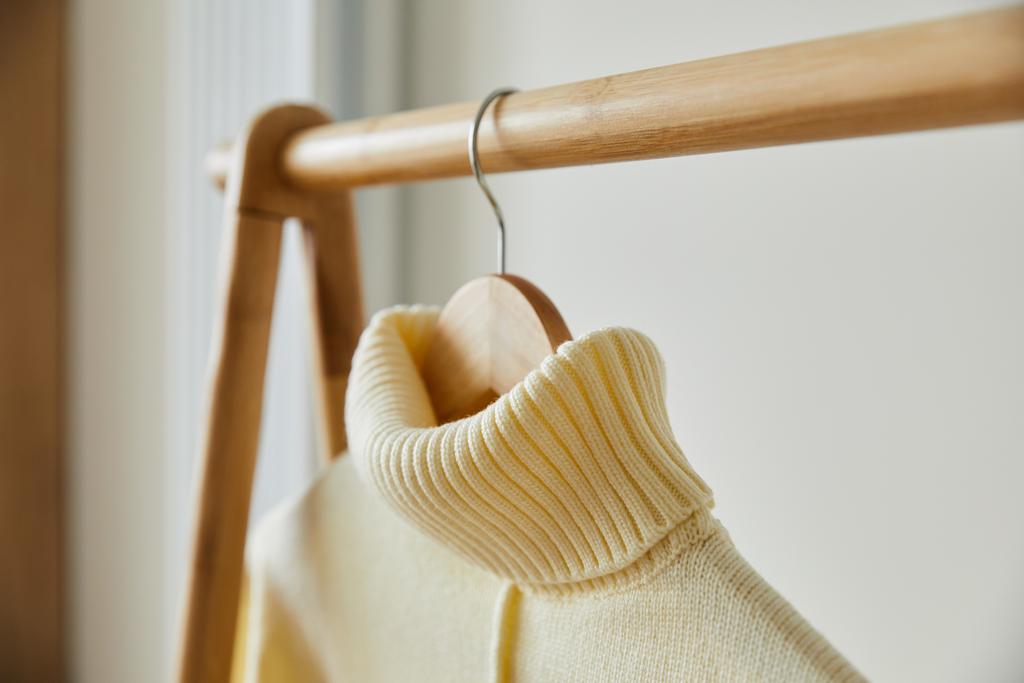 Nahaufnahme von beige gestricktem weichem Pullover, der auf einem hölzernen Kleiderbügel hängt, isoliert auf weiß - Foto, Bild