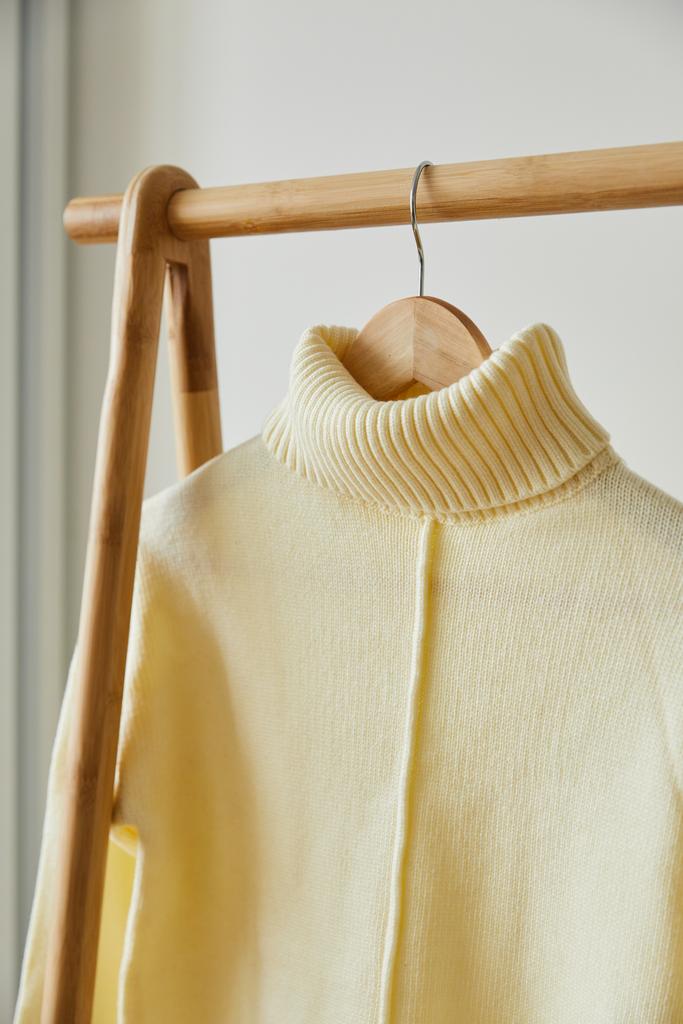 крупним планом бежевий в'язаний м'який светр, що висить на дерев'яній вішалці ізольовано на білому
 - Фото, зображення