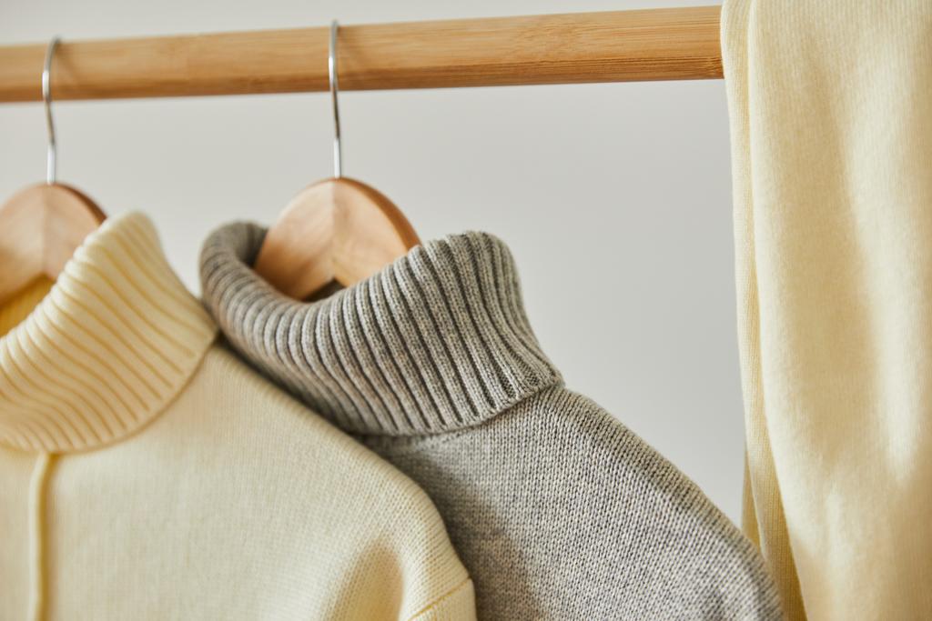 Nahaufnahme von beige und grau gestrickten weichen Pullovern, die auf hölzernen Kleiderbügeln isoliert auf weiß hängen - Foto, Bild