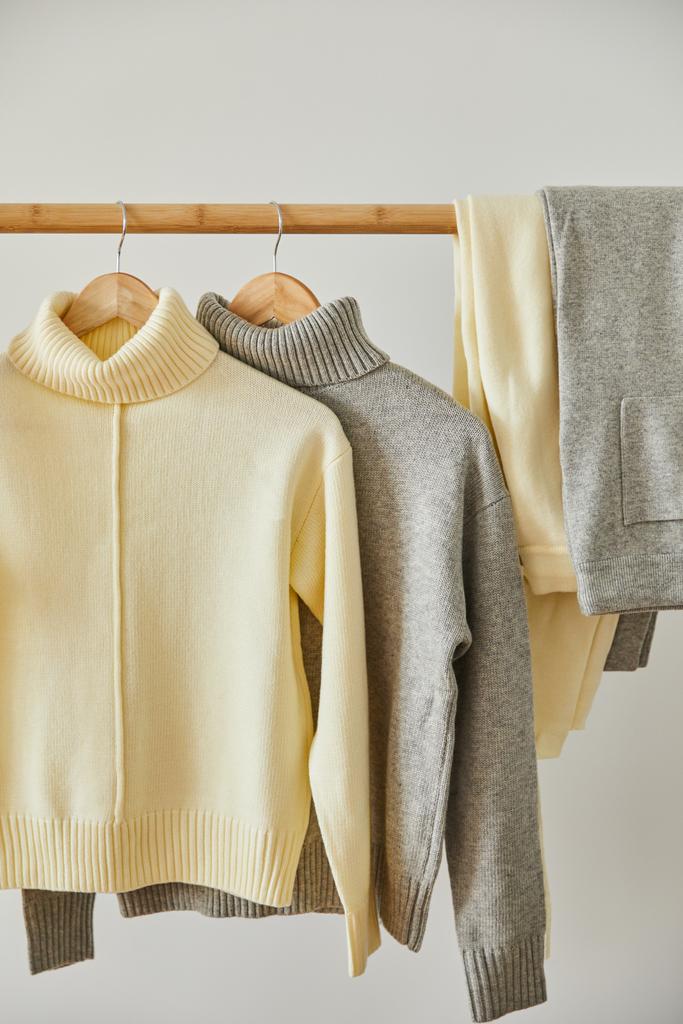 beige und grau gestrickte weiche Pullover und Hosen hängen an hölzernen Kleiderbügeln isoliert auf weiß - Foto, Bild