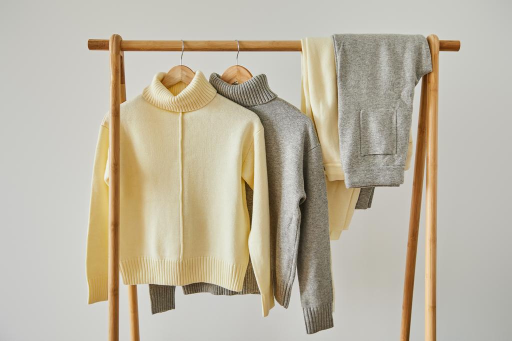 jerséis y pantalones suaves de punto beige y gris que cuelgan de perchas de madera aisladas en blanco
 - Foto, imagen